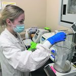 A female scientist wearing a lab coat, blue rubber gloves and a surgical mask, works in the Canadian Grain Commission's lab in WInnipeg.