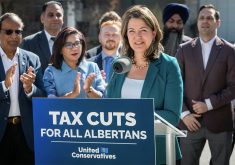 Alberta premier Danielle Smith stands behind a podium with a sign on it touting, "Tax cuts for all Albertans."