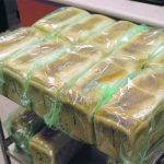 Loaves of freshly-baked bread wrapped in plastic and stacked on a cart.