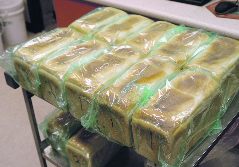 Loaves of freshly-baked bread wrapped in plastic and stacked on a cart.