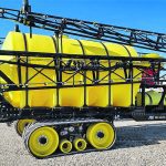 a large ,yellow, tow-behind agricultural sprayer with very long booms folded against its sides. The rig rides on tracks.