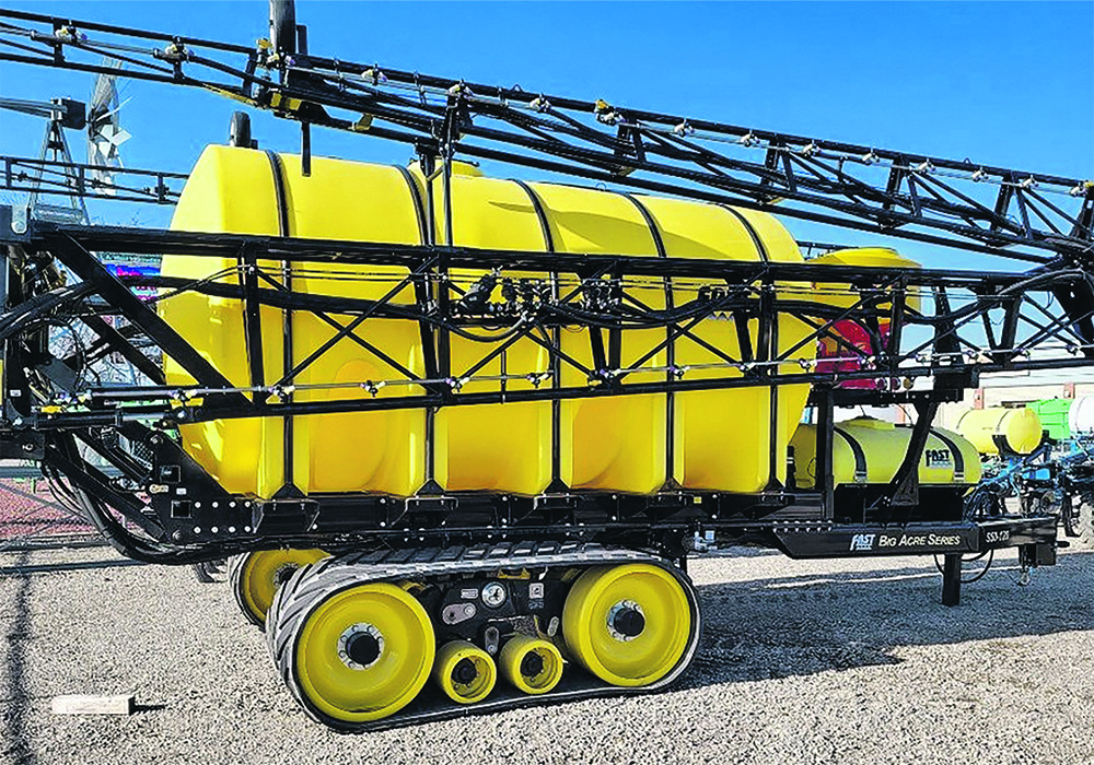 a large ,yellow, tow-behind agricultural sprayer with very long booms folded against its sides. The rig rides on tracks.