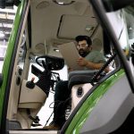 A man sits in the cab of a new tractor looking at a clipboard as he works to diagnose a problem with the machine.