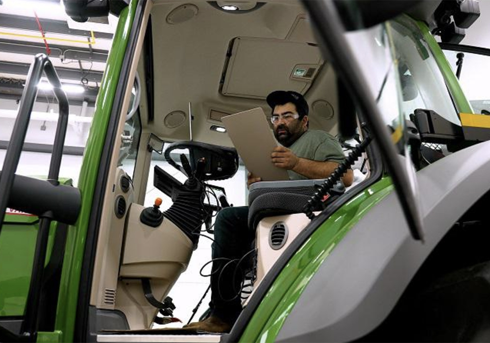 A man sits in the cab of a new tractor looking at a clipboard as he works to diagnose a problem with the machine.