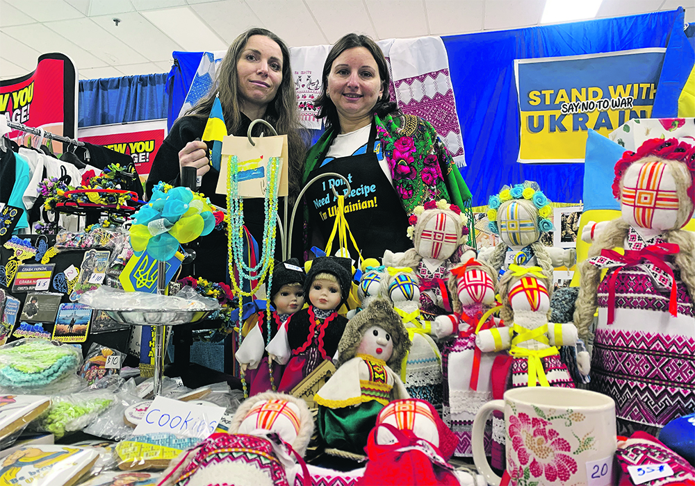 Two Ukrainian women, Olga Boiko and Liudmyla Todorova, stand behind their table full of baked goods, homemade dolls and beaded necklaces they're selling at the Royal Manitoba Winter Fair in Brandon to support the Ukraininan war effort.