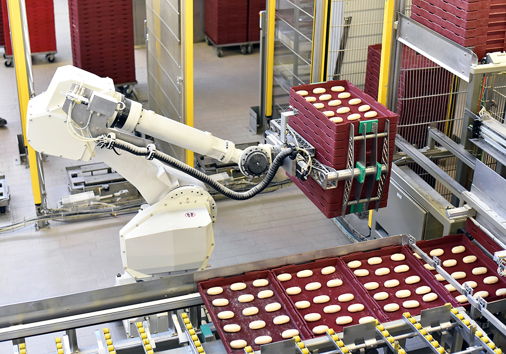 A robot moves a stack of trays with baked goods on them.