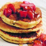 A stack of pancackes with syrup and bits of fruit on top,