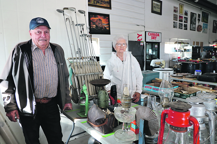 An older couple stand inside a garage surrounded by items to be sold at auction.