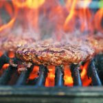 Close-up of a burger on a grill with flames surrounding the burger patty.