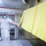 A man checks large noodles in an industrial pasta-making facility.