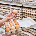 A shopper pulls an egg from its carton and examines it in an aisle in a grocery store.