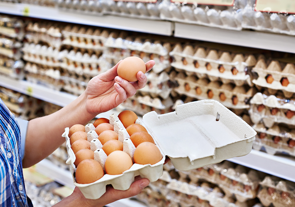A shopper pulls an egg from its carton and examines it in an aisle in a grocery store.