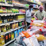 Two men look at products on that shelves in an aisle in a grocery story in India.