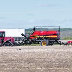 An air seeder is being pulled by a massive, tracked tractor.