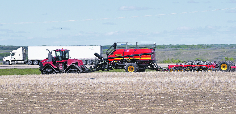 An air seeder is being pulled by a massive, tracked tractor.