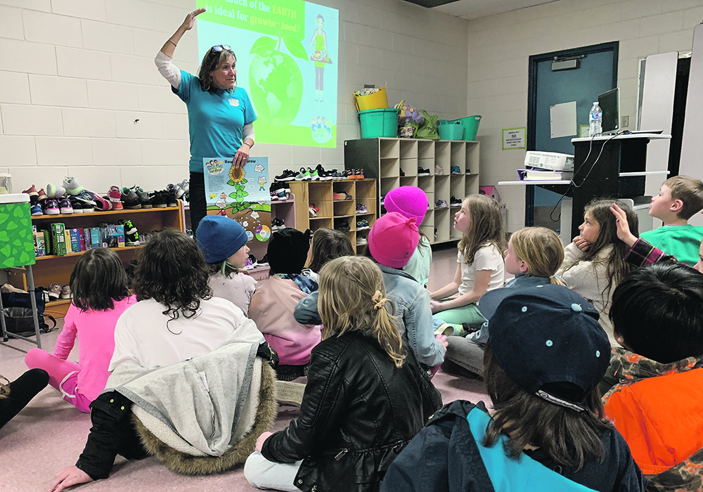 A teacher stands at the front of the classroom talking to young students.