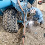 A man is welding on a piece of farm machinery.