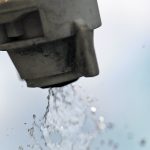Close-up of a sprayer's nozzle tip with clear liquid coming out.