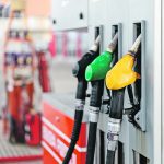 Three different coloured nozzles hang from a gas pump at a gas station.