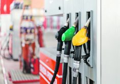 Three different coloured nozzles hang from a gas pump at a gas station.