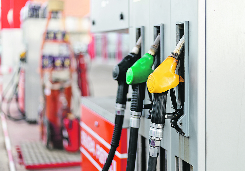 Three different coloured nozzles hang from a gas pump at a gas station.