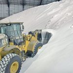 A wheel loader scoops up a bucket full of urea fertilizer from a massive pile in an indoor warehouse.