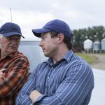 An older farmer and his twenty-something son chat on the farm.