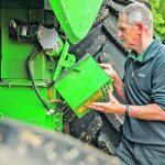 A farmer installs a new pieces of equipment on his green combine.