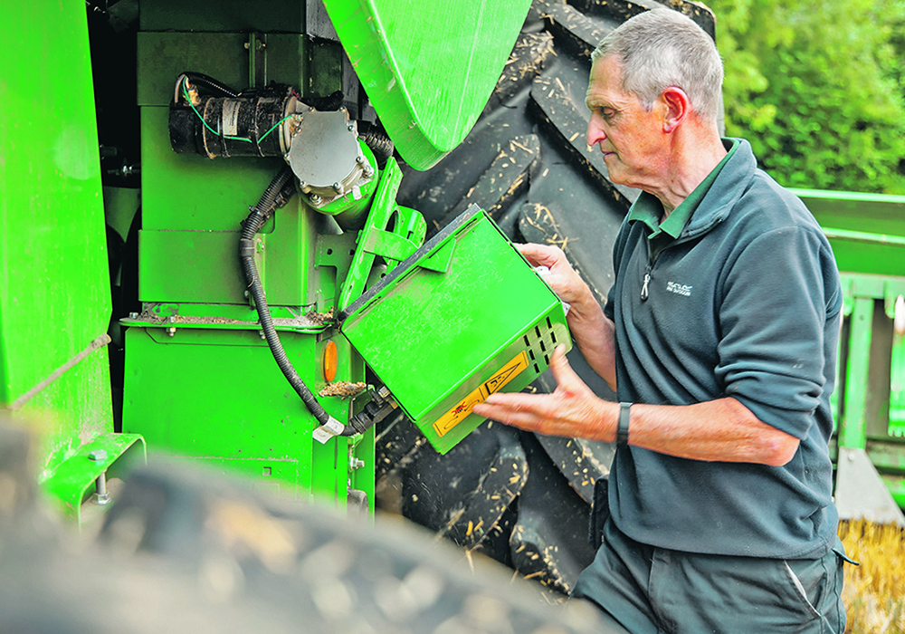 A farmer installs a new pieces of equipment on his green combine.