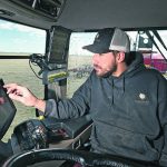A farmer taps on a touch screen mounted inside the cab of his tractor.