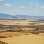 An aerial view of the patchwork of prairie crops with the Rocky Mountains in the background.