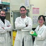 Three scientists in lab coats pose in alab.
