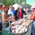 Three women look at some garlic cloves on a table at a farmers' market.