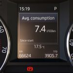 A car dashboard showing "7.4 litres per 100 km" on the fuel economy screen.