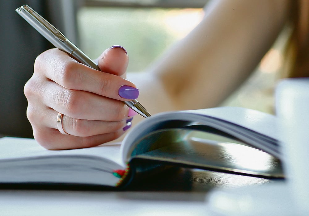 A woman's hand is holding a pen, recording information in a journal of some sort.