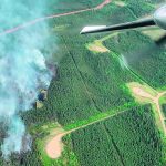 An aerial photo of a forest fire in Alberta, the plane's wing and a propeller are visible.