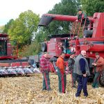 Ukrainian men gather around several combines as they prepare to harvest during a war.