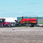 A large, tracked tractor pulls an air seeder rig near the highway on the Discovery Farm near Langham, Sask.