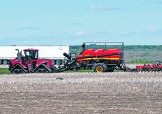 A large, tracked tractor pulls an air seeder rig near the highway on the Discovery Farm near Langham, Sask.