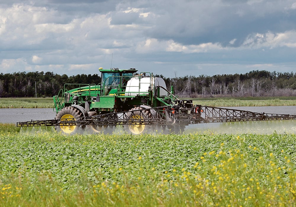 A sprayer moves through a crop with mist visible beneath its booms.