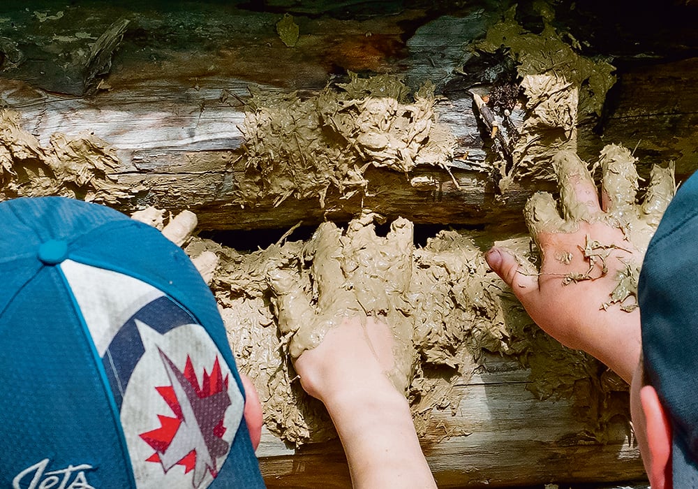 Two students chink a log house with clay, straw and dried horse manure.