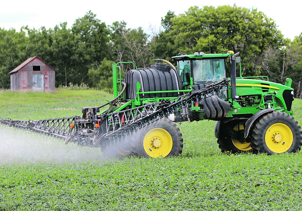 An agricultural high-clearance sprayer is seen spraying a lush, green crop.
