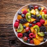 A bowl filled with cut-up fruit of all colours and varieties.