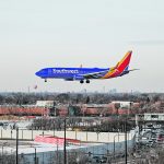A blue commercial jetliner is about to land at a large airport.