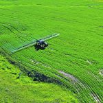 Drone shot of a farmer spraying herbicide on a barley crop.