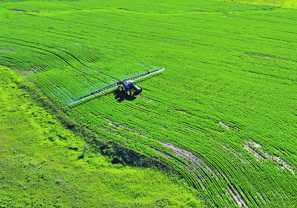 Drone shot of a farmer spraying herbicide on a barley crop.