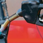 A commercial gas nozzle is seen pumping fuel into a red tractor.