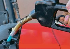 A commercial gas nozzle is seen pumping fuel into a red tractor.