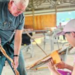 Journey Froese sands her walking stick using sand paper as Greg Mallett shows her how smooth the branch needs to be during a recent workshop.