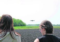 Over-the-shoulder-shot of two students watching a drone over a farm field in Manitoba.